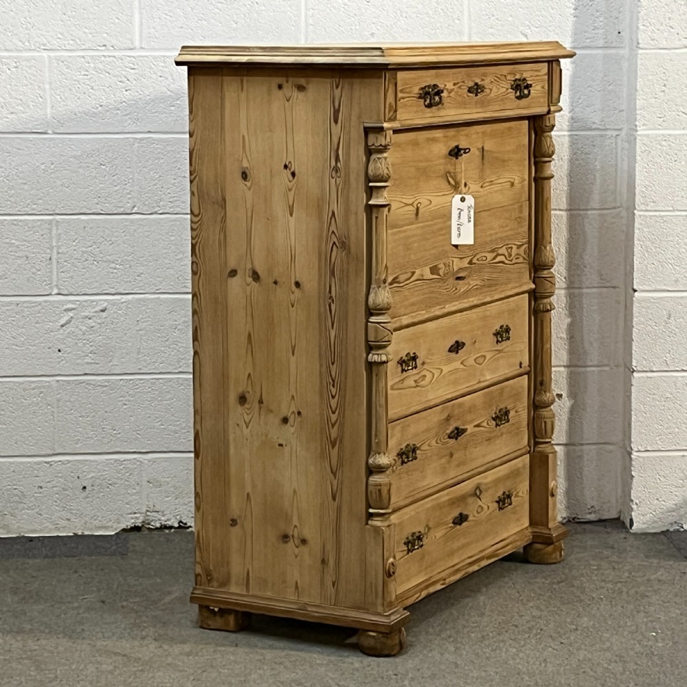 An antique pine secretaire desk featuring a fall-front writing compartment above multiple drawers, decorated with turned side columns and dark metal handles. View III
