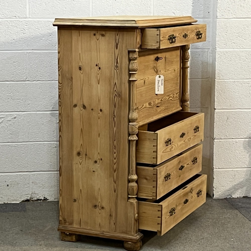 An antique pine secretaire desk featuring a fall-front writing compartment above multiple drawers, decorated with turned side columns and dark metal handles. View VIII