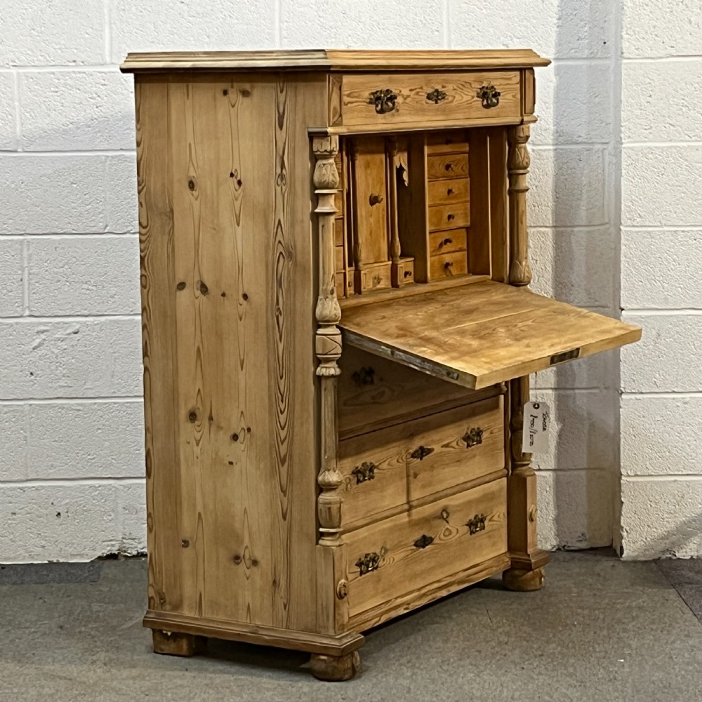An antique pine secretaire desk featuring a fall-front writing compartment above multiple drawers, decorated with turned side columns and dark metal handles. View IX