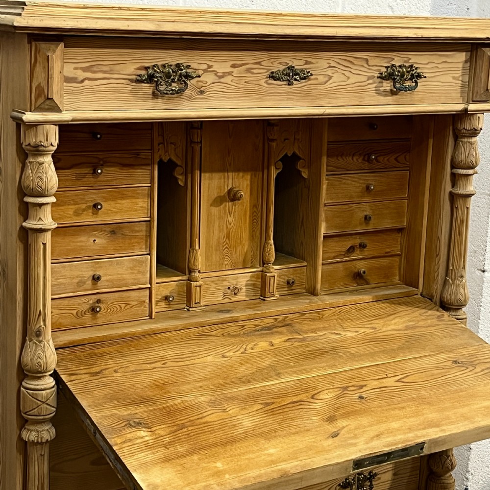 An antique pine secretaire desk featuring a fall-front writing compartment above multiple drawers, decorated with turned side columns and dark metal handles. View XI