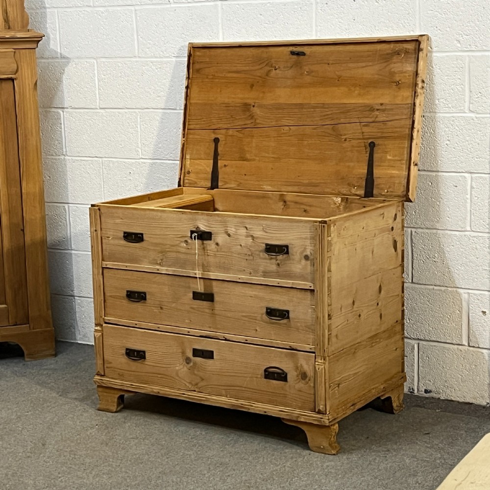A large natural pine mule chest featuring an open hinged lid above lower drawers with dark metal pull handles and bracket feet. View V