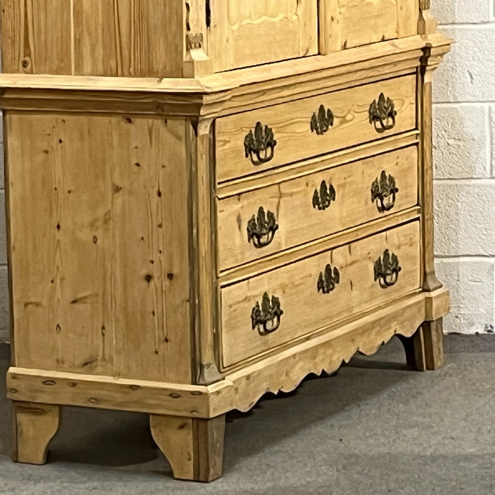 A tall two-part natural pine linen press featuring a double-door top cupboard over three drawers with brass drop handles. View II