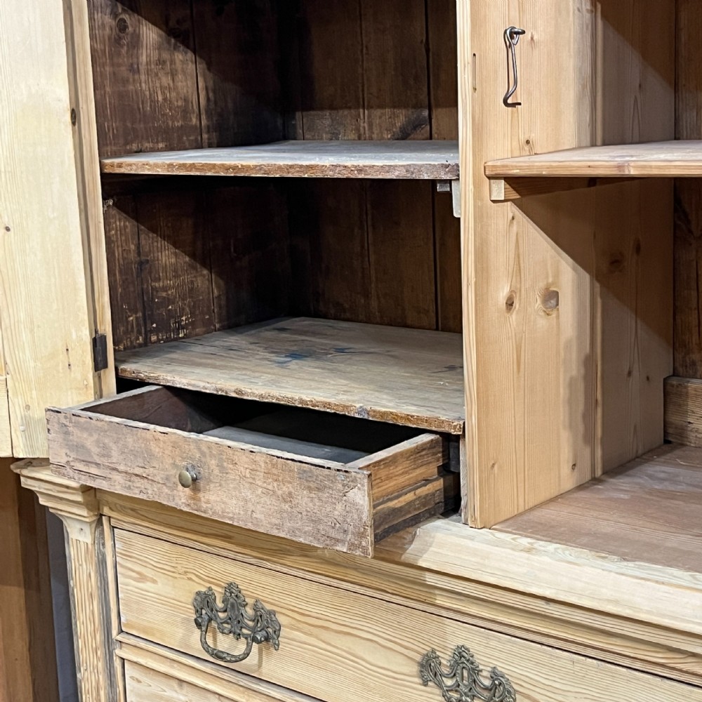 A tall two-part natural pine linen press featuring a double-door top cupboard over three drawers with brass drop handles. View IX