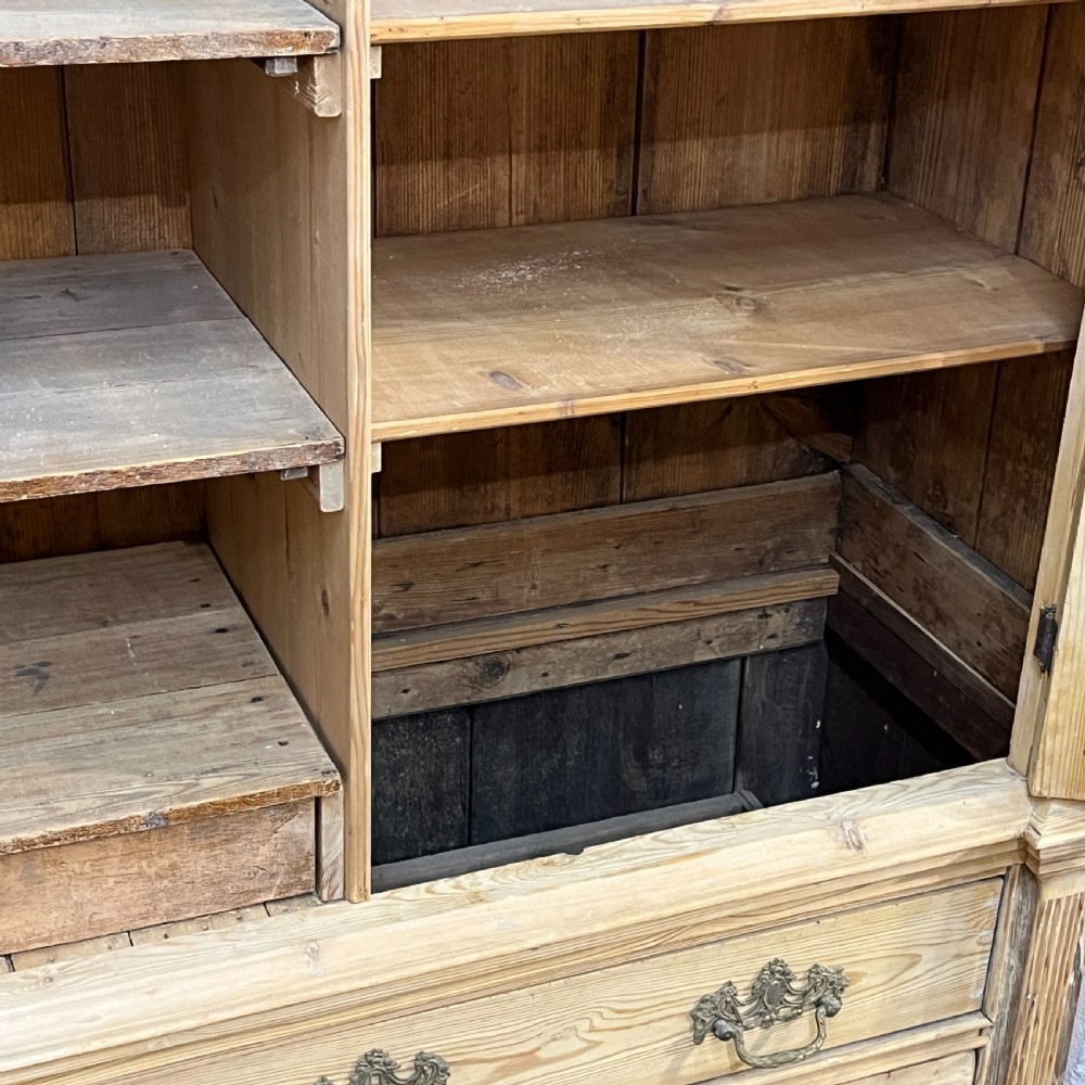 A tall two-part natural pine linen press featuring a double-door top cupboard over three drawers with brass drop handles. View XI