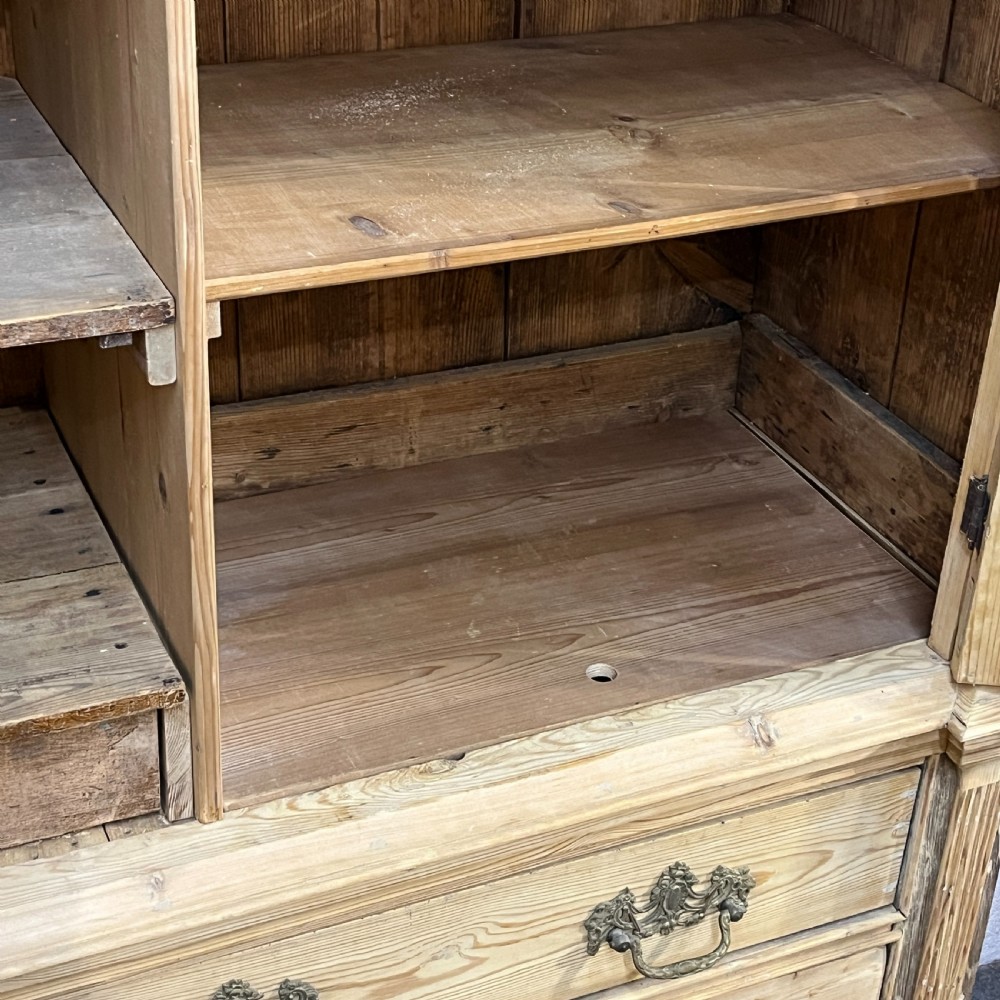 A tall two-part natural pine linen press featuring a double-door top cupboard over three drawers with brass drop handles. View XII