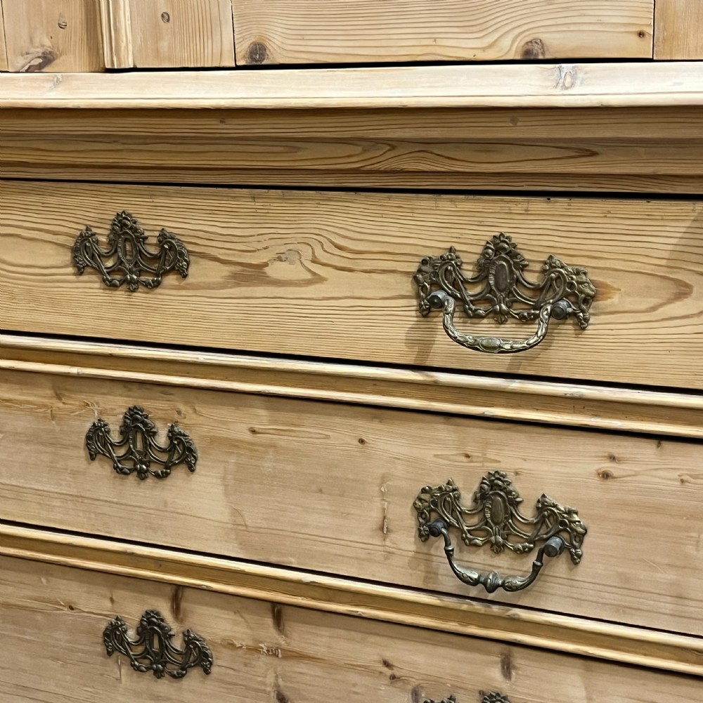 A tall two-part natural pine linen press featuring a double-door top cupboard over three drawers with brass drop handles. View XIII