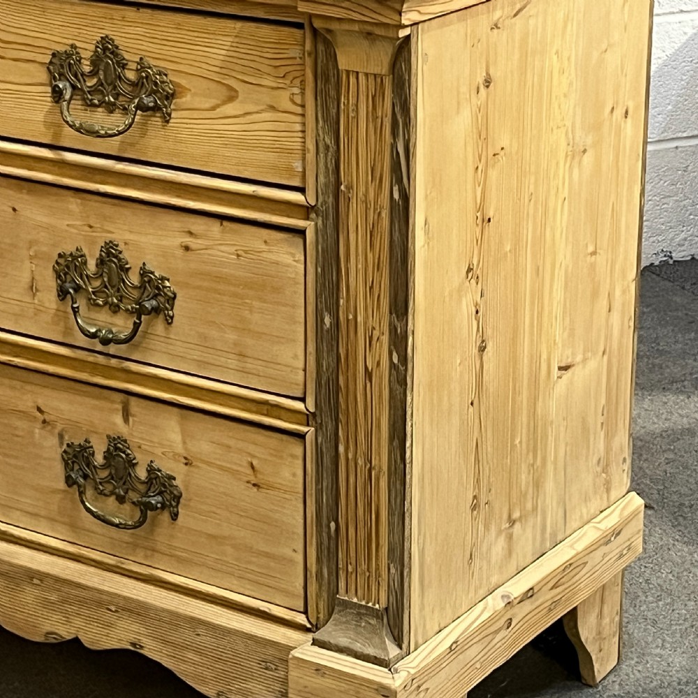 A tall two-part natural pine linen press featuring a double-door top cupboard over three drawers with brass drop handles. View XV