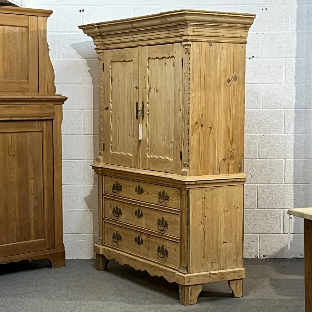 A tall two-part natural pine linen press featuring a double-door top cupboard over three drawers with brass drop handles. View XVI