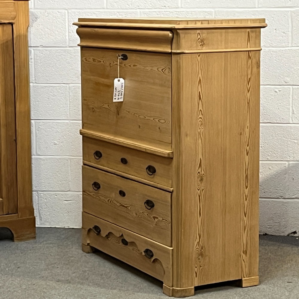 A tall antique stripped pine secretaire bureau featuring a upper fall-front writing flap above three long drawers with brass handles and a carved lower apron. View II