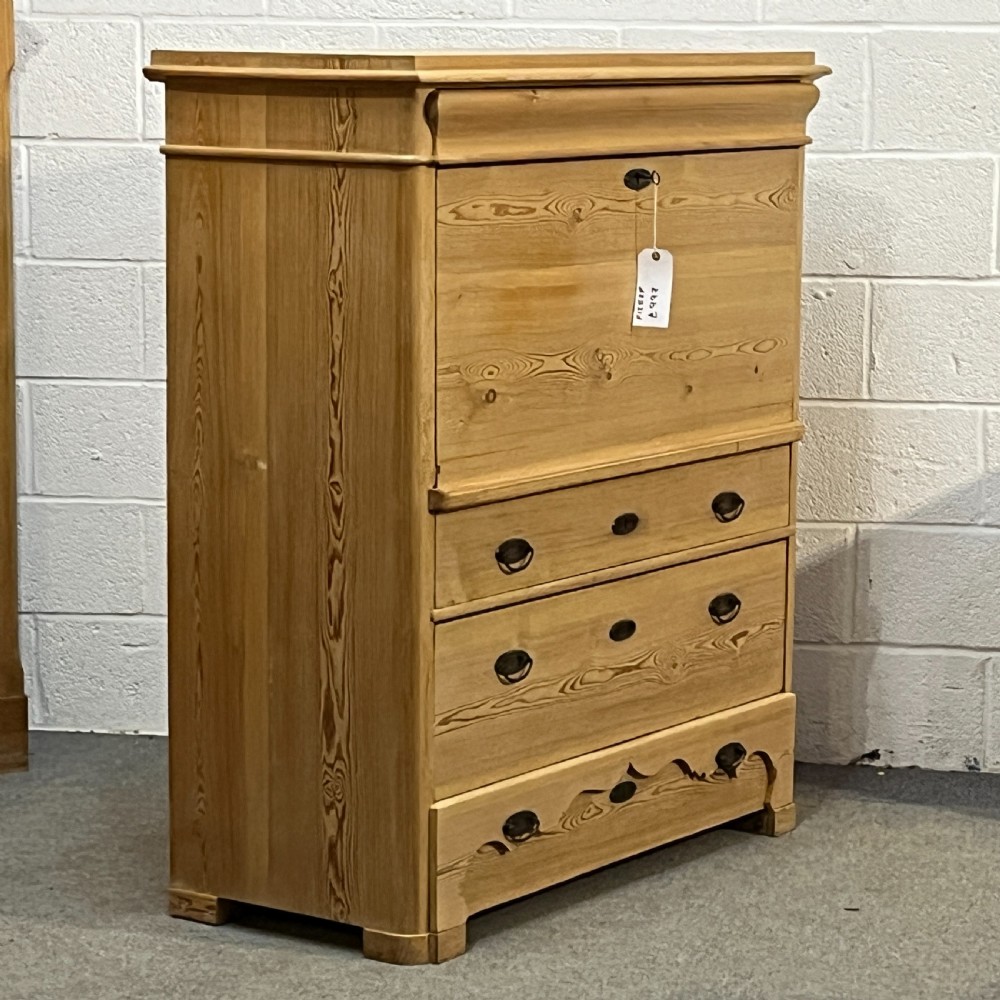 A tall antique stripped pine secretaire bureau featuring a upper fall-front writing flap above three long drawers with brass handles and a carved lower apron. View III