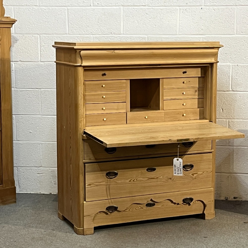 A tall antique stripped pine secretaire bureau featuring a upper fall-front writing flap above three long drawers with brass handles and a carved lower apron. View IV