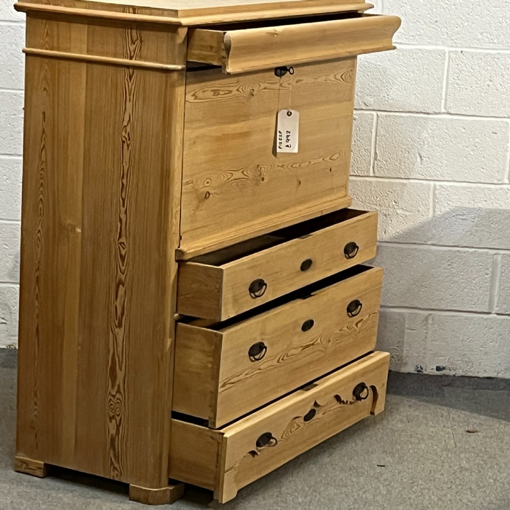 A tall antique stripped pine secretaire bureau featuring a upper fall-front writing flap above three long drawers with brass handles and a carved lower apron. View V