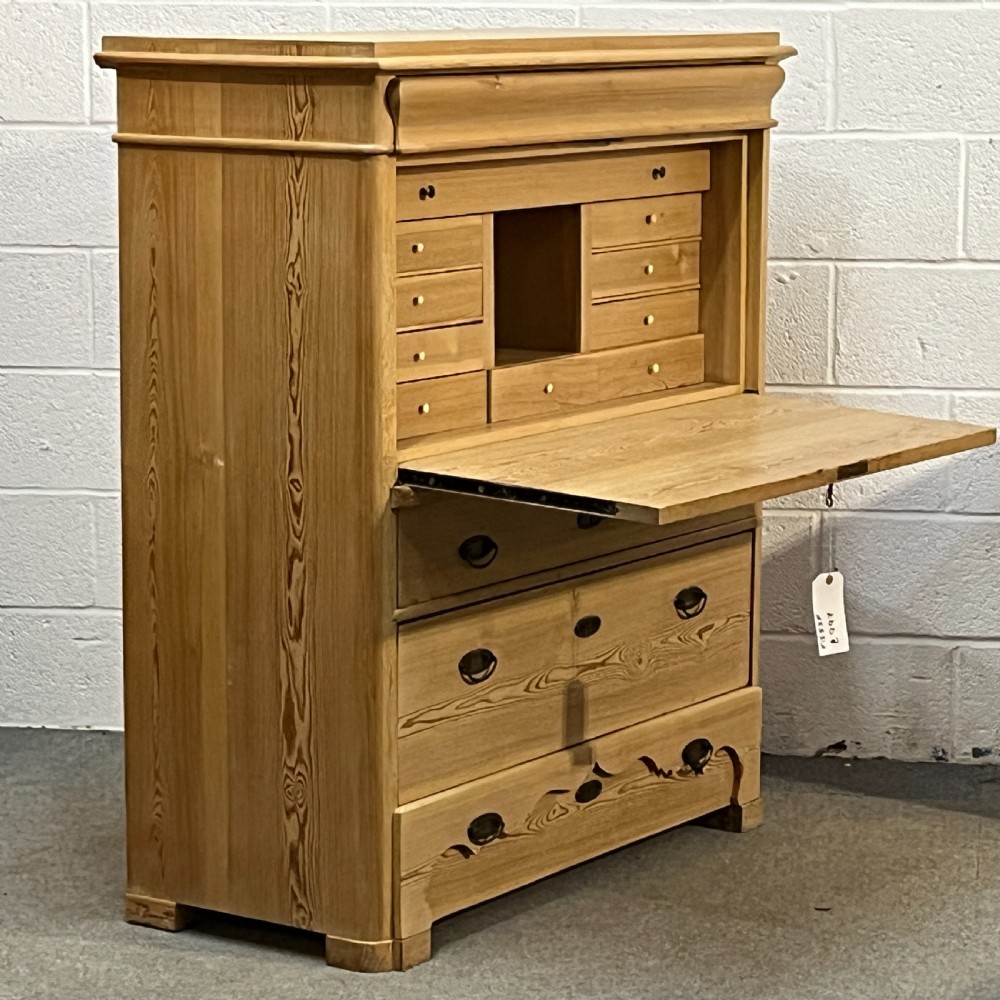 A tall antique stripped pine secretaire bureau featuring a upper fall-front writing flap above three long drawers with brass handles and a carved lower apron. View VI