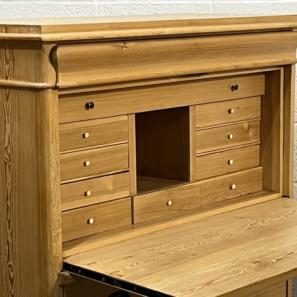 A tall antique stripped pine secretaire bureau featuring a upper fall-front writing flap above three long drawers with brass handles and a carved lower apron. View VIII