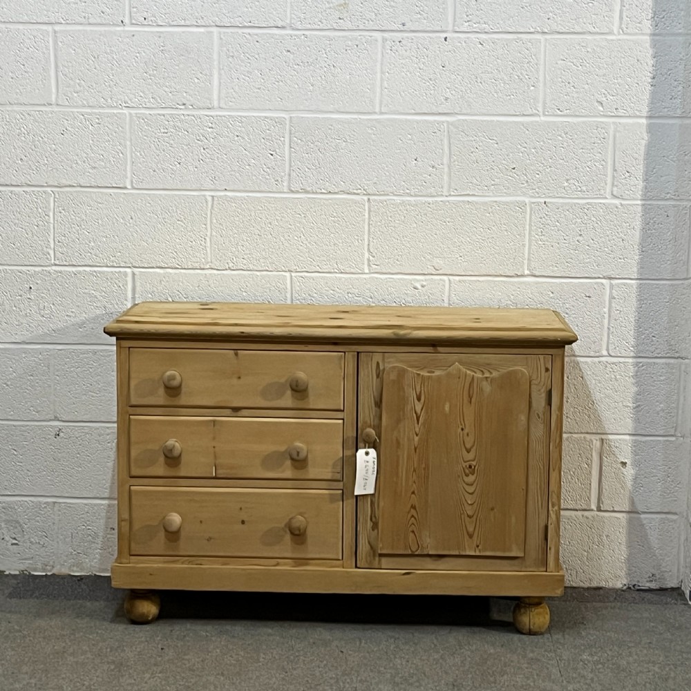 A small Edwardian pine chiffonier featuring three drawers on the left with turned wooden knob handles, a single panelled cupboard door on the right, and rounded bun feet.