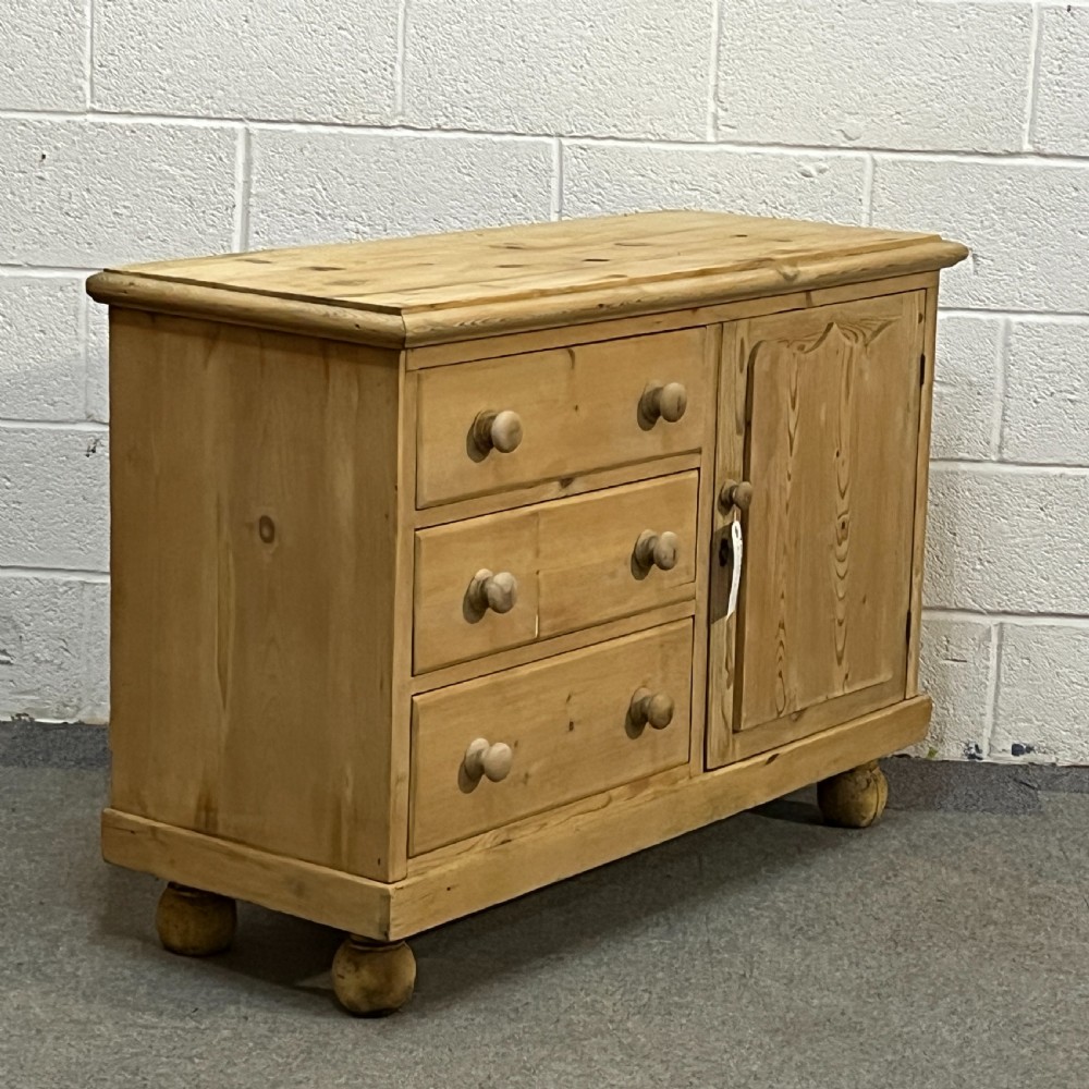 A small Edwardian pine chiffonier featuring three drawers on the left with turned wooden knob handles, a single panelled cupboard door on the right, and rounded bun feet. View III