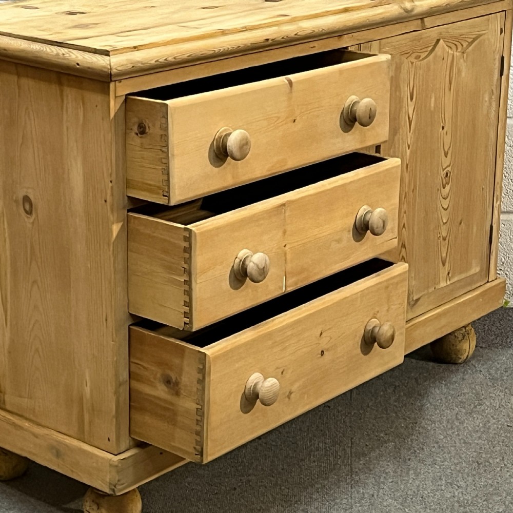 A small Edwardian pine chiffonier featuring three drawers on the left with turned wooden knob handles, a single panelled cupboard door on the right, and rounded bun feet. View VII