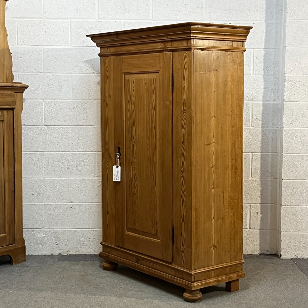 A tall antique waxed pine storage cupboard featuring a single panelled door, an iron keyhole escutcheon, a moulded top cornice, and bun feet. View II