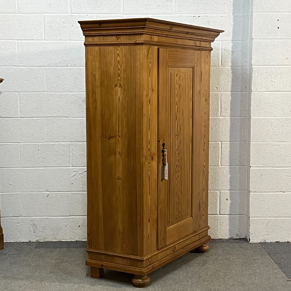 A tall antique waxed pine storage cupboard featuring a single panelled door, an iron keyhole escutcheon, a moulded top cornice, and bun feet. View III