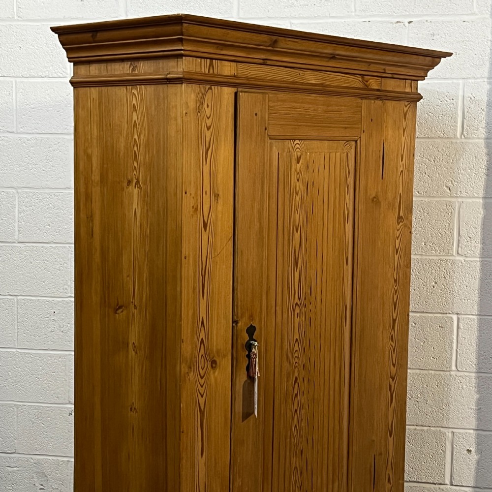 A tall antique waxed pine storage cupboard featuring a single panelled door, an iron keyhole escutcheon, a moulded top cornice, and bun feet. View IV