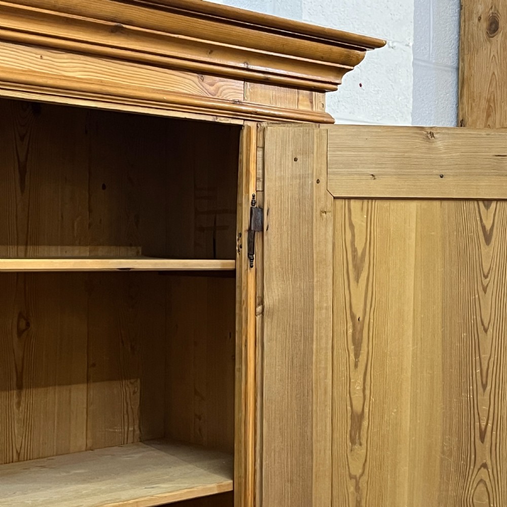 A tall antique waxed pine storage cupboard featuring a single panelled door, an iron keyhole escutcheon, a moulded top cornice, and bun feet. View VII