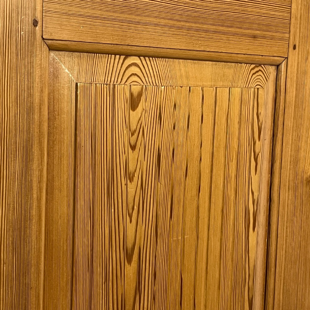 A tall antique waxed pine storage cupboard featuring a single panelled door, an iron keyhole escutcheon, a moulded top cornice, and bun feet. View VIII