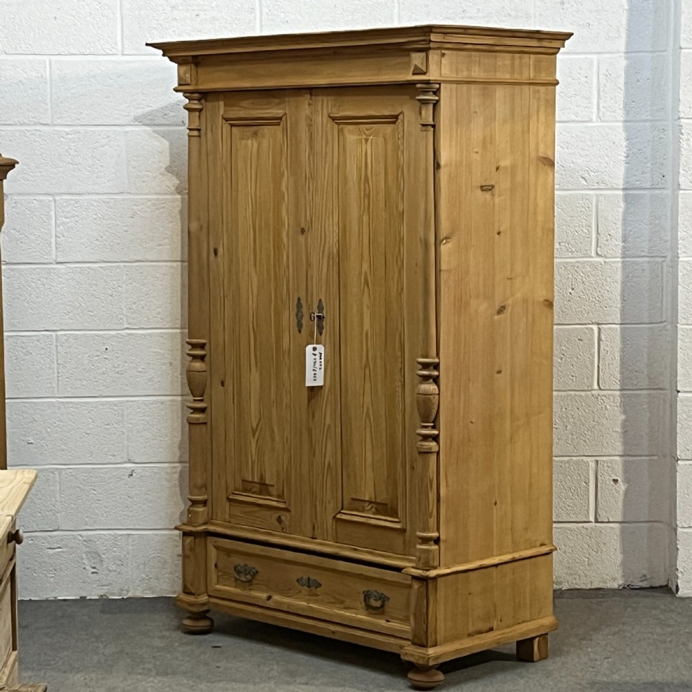 A freestanding double-door antique pine wardrobe featuring turned front columns, panelled doors, key escutcheons, and a single bottom drawer. View II