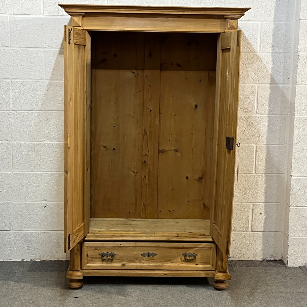 A freestanding double-door antique pine wardrobe featuring turned front columns, panelled doors, key escutcheons, and a single bottom drawer. View IV