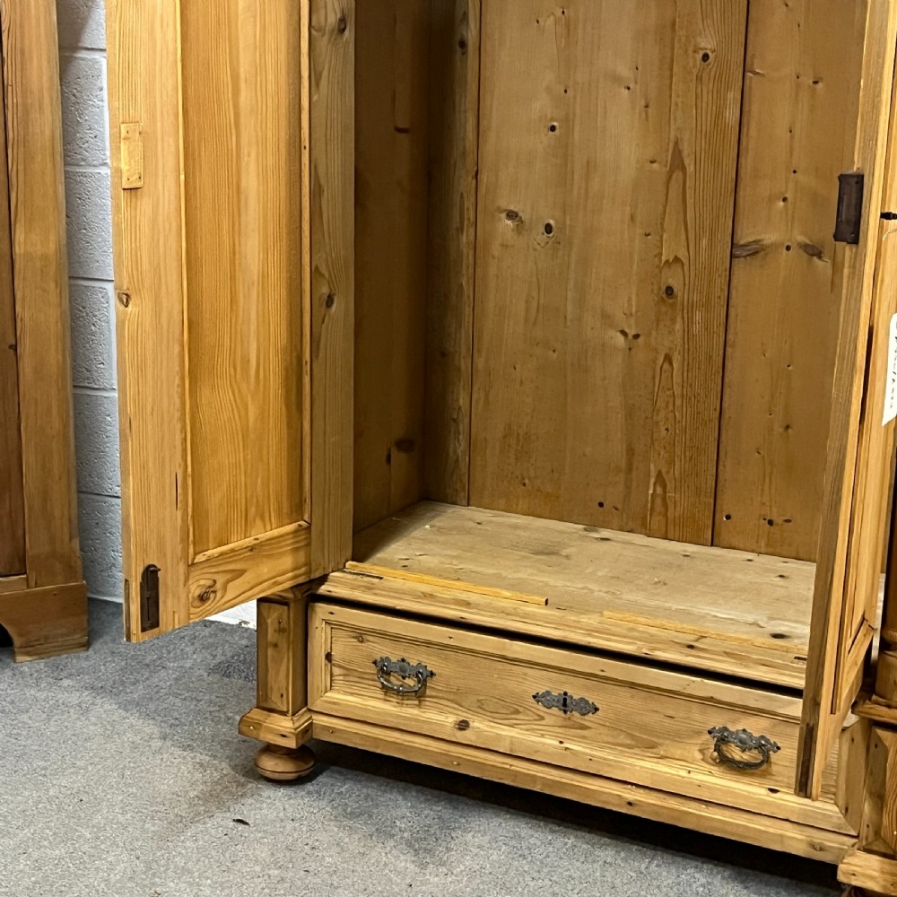 A freestanding double-door antique pine wardrobe featuring turned front columns, panelled doors, key escutcheons, and a single bottom drawer. View VII