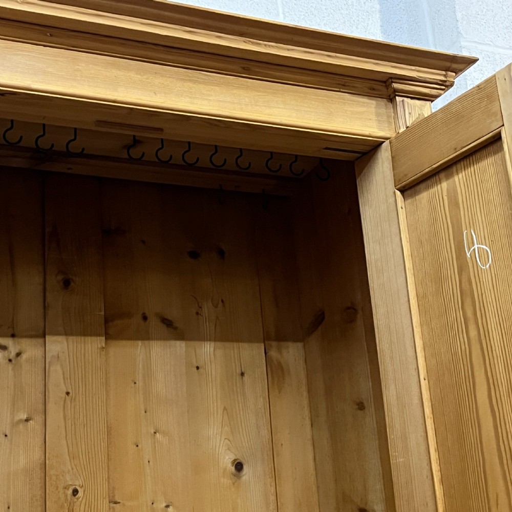 A freestanding double-door antique pine wardrobe featuring turned front columns, panelled doors, key escutcheons, and a single bottom drawer. View VIII