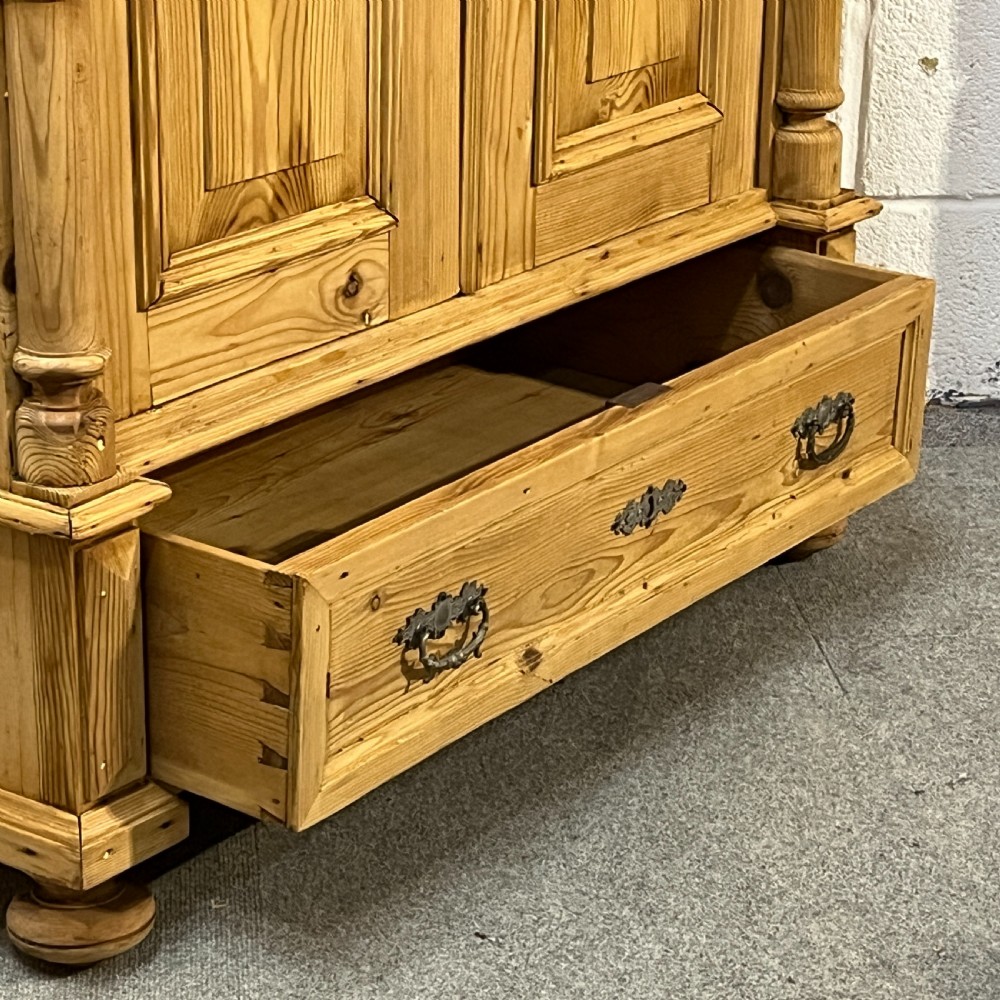 A freestanding double-door antique pine wardrobe featuring turned front columns, panelled doors, key escutcheons, and a single bottom drawer. View IX