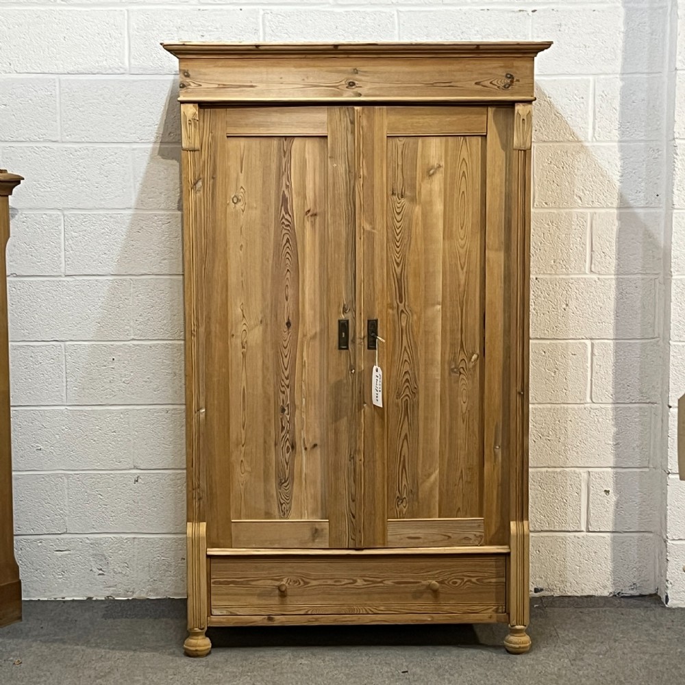 An antique pine wardrobe with two panelled doors, a single bottom drawer, turned bun feet, and a moulded top cornice.