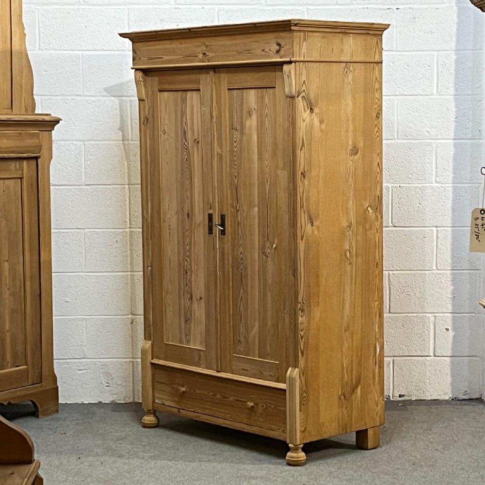 An antique pine wardrobe with two panelled doors, a single bottom drawer, turned bun feet, and a moulded top cornice. View II