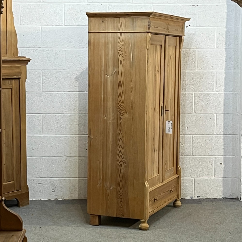 An antique pine wardrobe with two panelled doors, a single bottom drawer, turned bun feet, and a moulded top cornice. View III