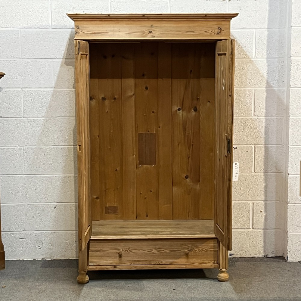 An antique pine wardrobe with two panelled doors, a single bottom drawer, turned bun feet, and a moulded top cornice. View IV