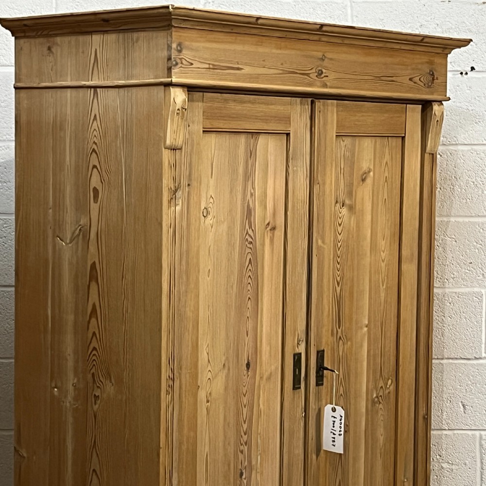 An antique pine wardrobe with two panelled doors, a single bottom drawer, turned bun feet, and a moulded top cornice. View V