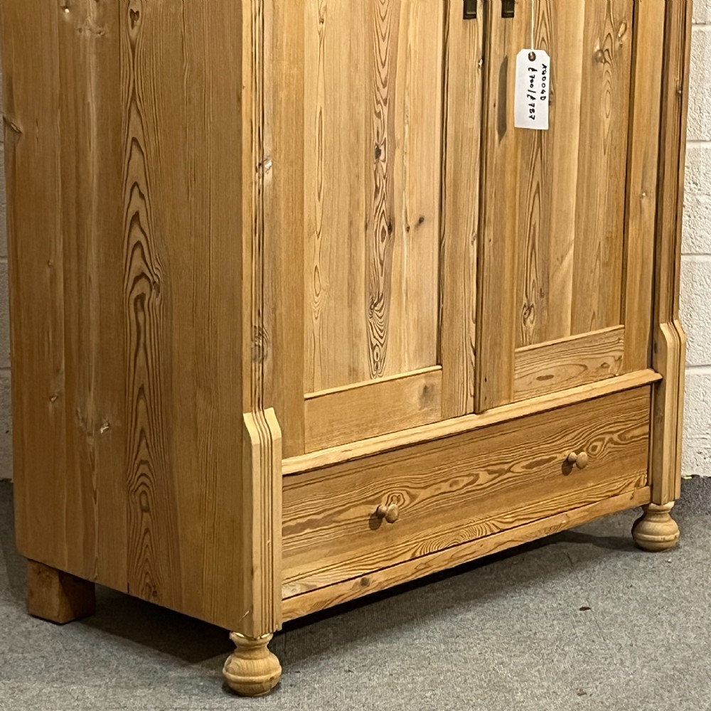An antique pine wardrobe with two panelled doors, a single bottom drawer, turned bun feet, and a moulded top cornice. View VI