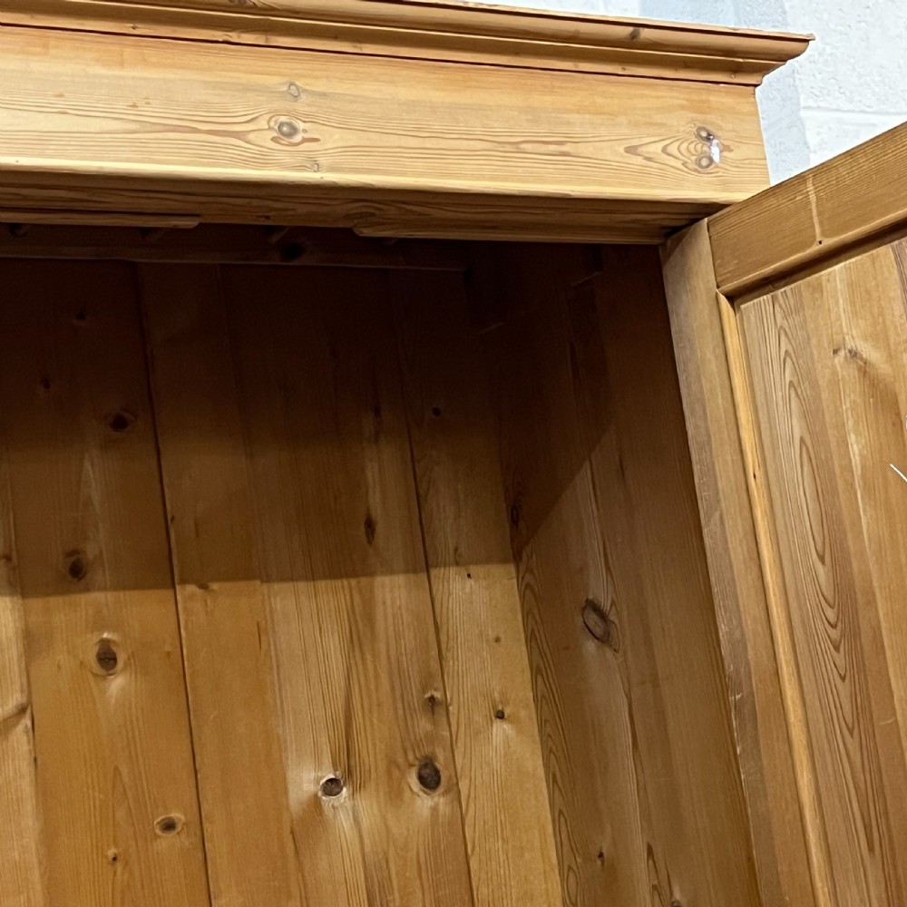 An antique pine wardrobe with two panelled doors, a single bottom drawer, turned bun feet, and a moulded top cornice. View VII
