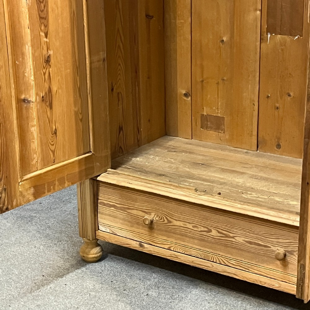An antique pine wardrobe with two panelled doors, a single bottom drawer, turned bun feet, and a moulded top cornice. View VIII