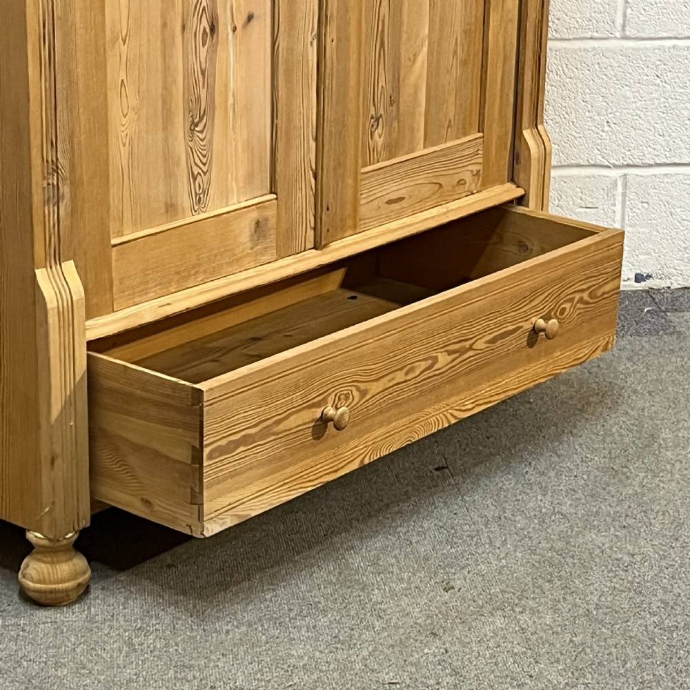 An antique pine wardrobe with two panelled doors, a single bottom drawer, turned bun feet, and a moulded top cornice. View IX