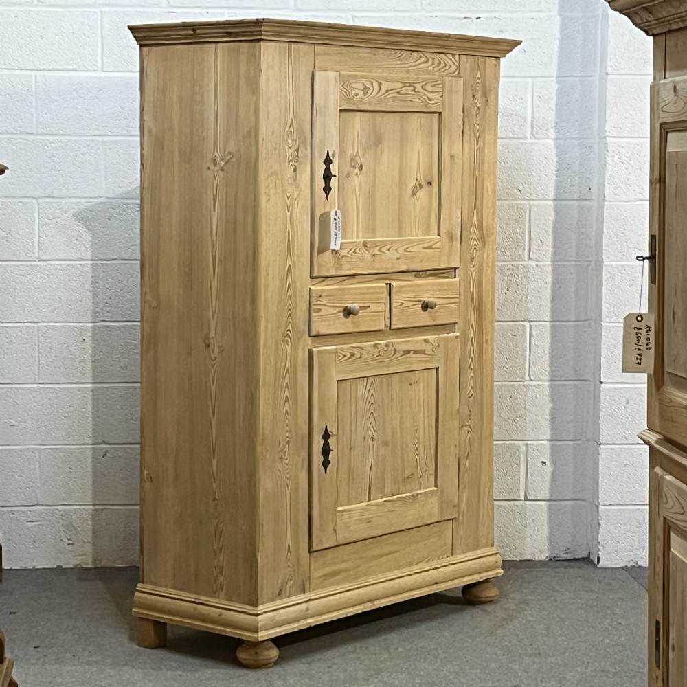 A tall stripped antique pine storage cupboard featuring two fielded panel doors, two central drawers, black iron escutcheons, and turned bun feet. View III