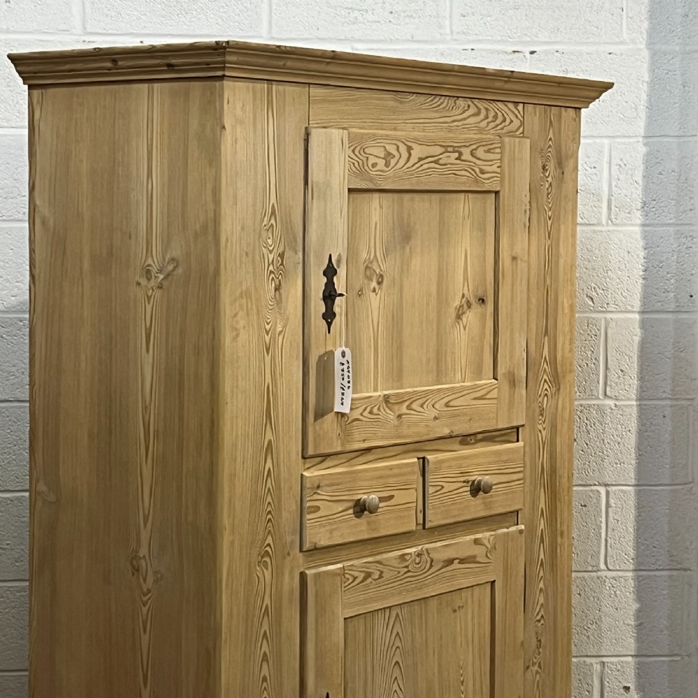 A tall stripped antique pine storage cupboard featuring two fielded panel doors, two central drawers, black iron escutcheons, and turned bun feet. View IV