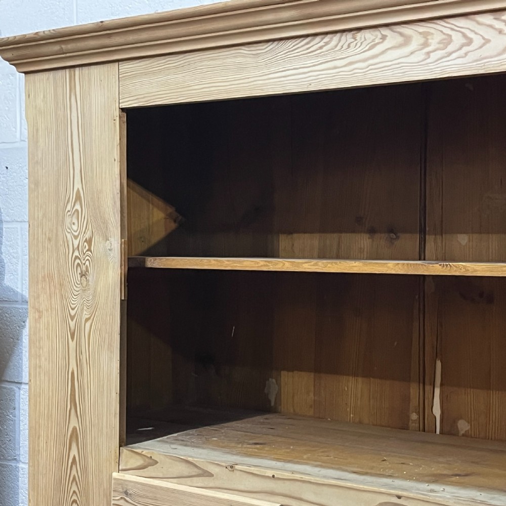 A tall stripped antique pine storage cupboard featuring two fielded panel doors, two central drawers, black iron escutcheons, and turned bun feet. View VII