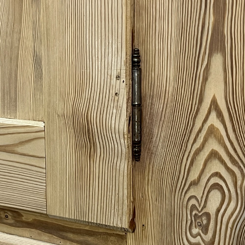 A tall stripped antique pine storage cupboard featuring two fielded panel doors, two central drawers, black iron escutcheons, and turned bun feet. View X