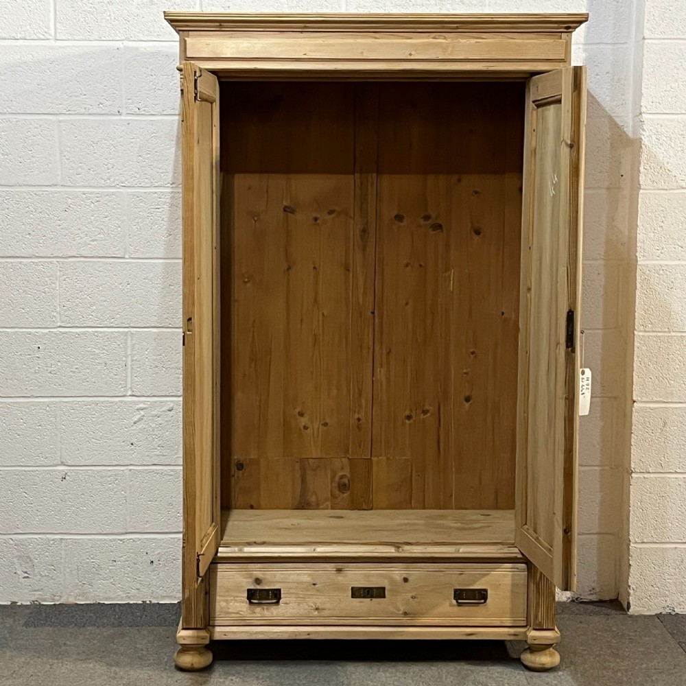 A stripped pine wardrobe featuring carved panel doors with Art Nouveau motifs, a lower drawer with brass handles, and turned bun feet. View IV