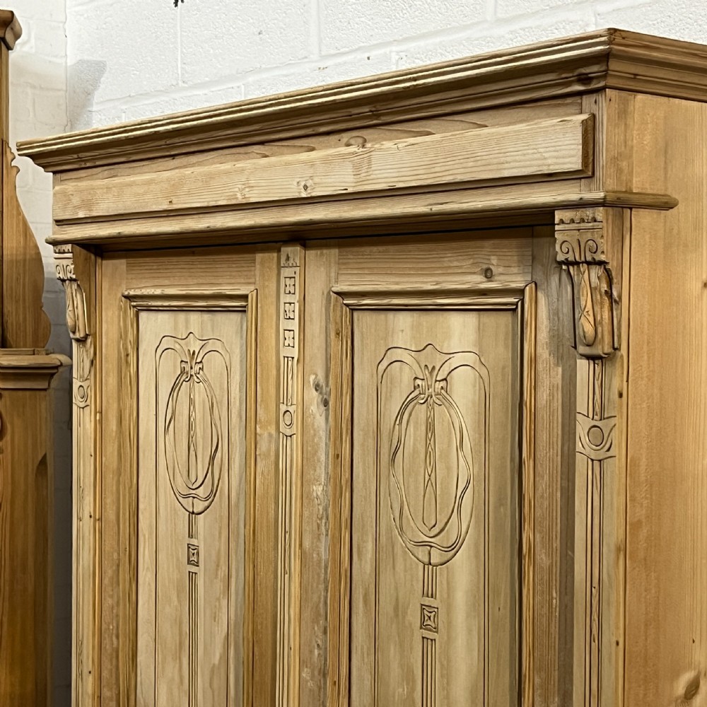 A stripped pine wardrobe featuring carved panel doors with Art Nouveau motifs, a lower drawer with brass handles, and turned bun feet. View VIII