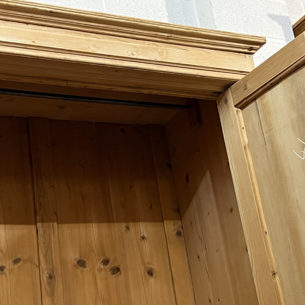 A stripped pine wardrobe featuring carved panel doors with Art Nouveau motifs, a lower drawer with brass handles, and turned bun feet. View X