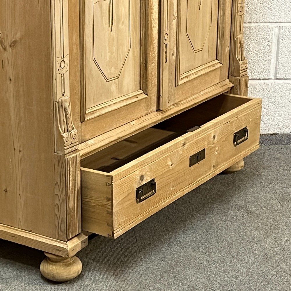 A stripped pine wardrobe featuring carved panel doors with Art Nouveau motifs, a lower drawer with brass handles, and turned bun feet. View XII
