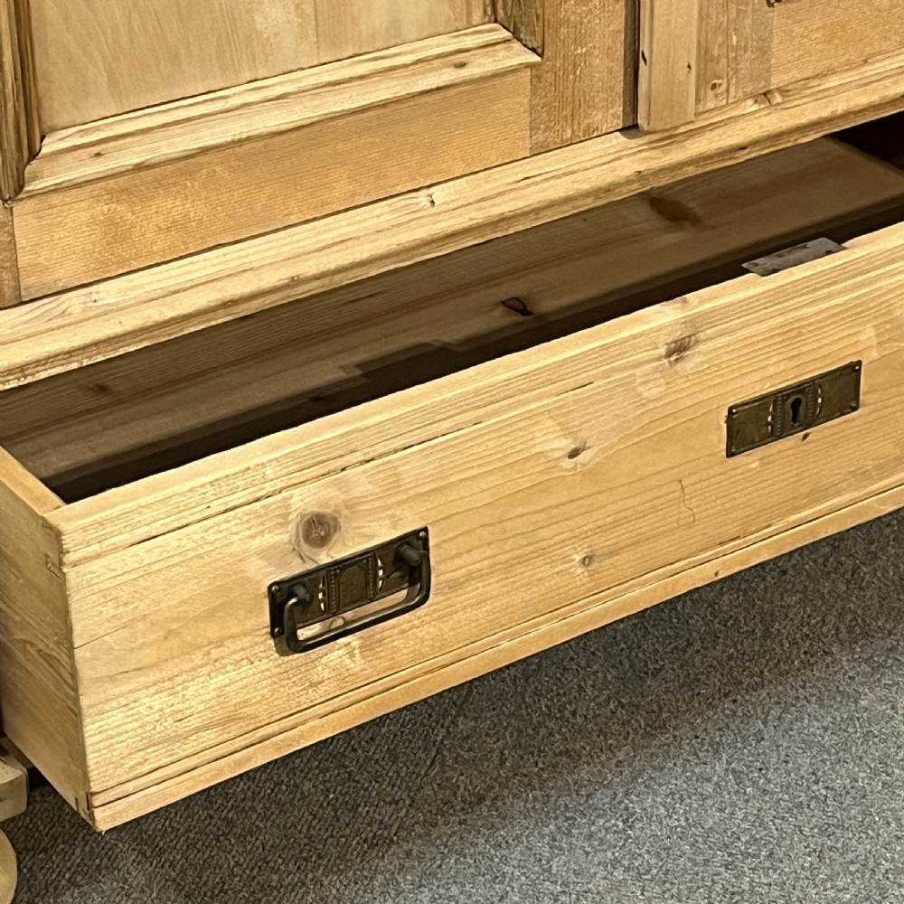 A stripped pine wardrobe featuring carved panel doors with Art Nouveau motifs, a lower drawer with brass handles, and turned bun feet. View XIII