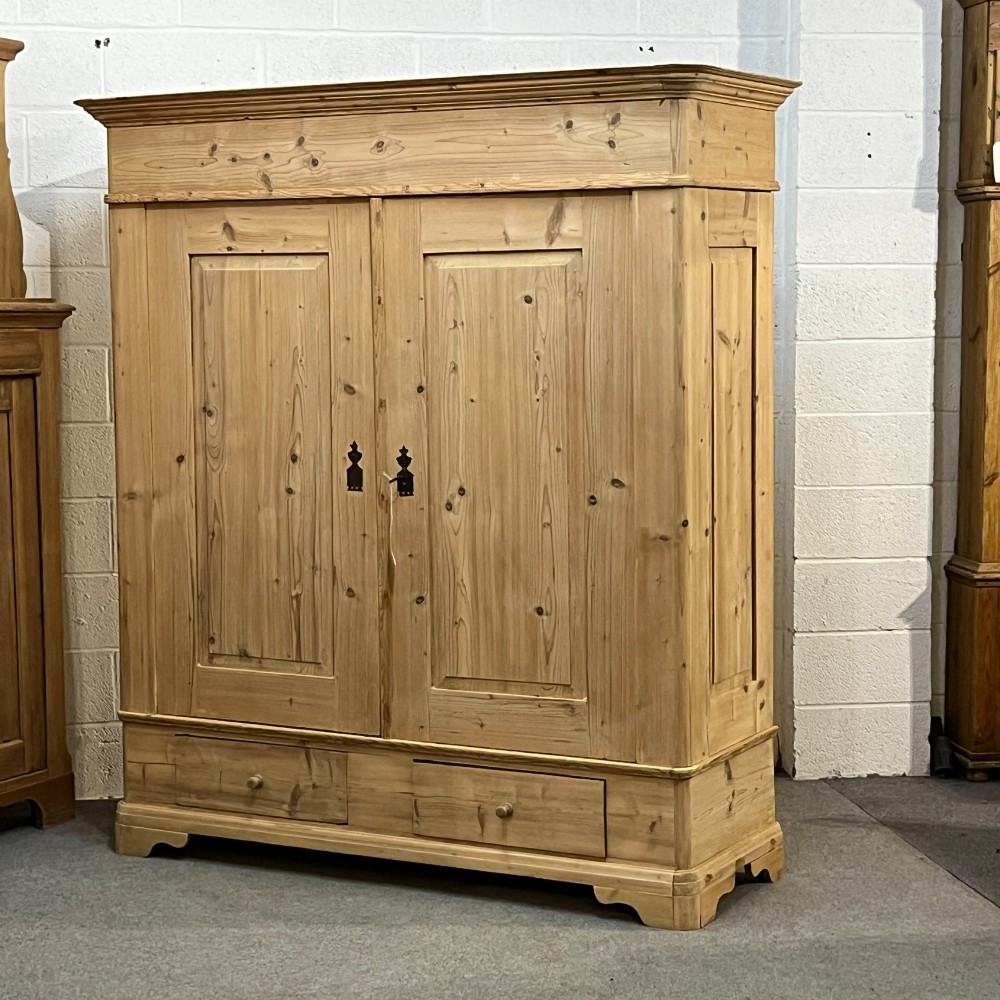 A large Victorian pine double wardrobe featuring fielded panel doors, iron escutcheons, and two base drawers on a plinth foundation. View II